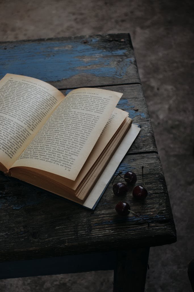 A vintage book open on a rustic wooden table with cherries, creating a classic and nostalgic atmosphere.