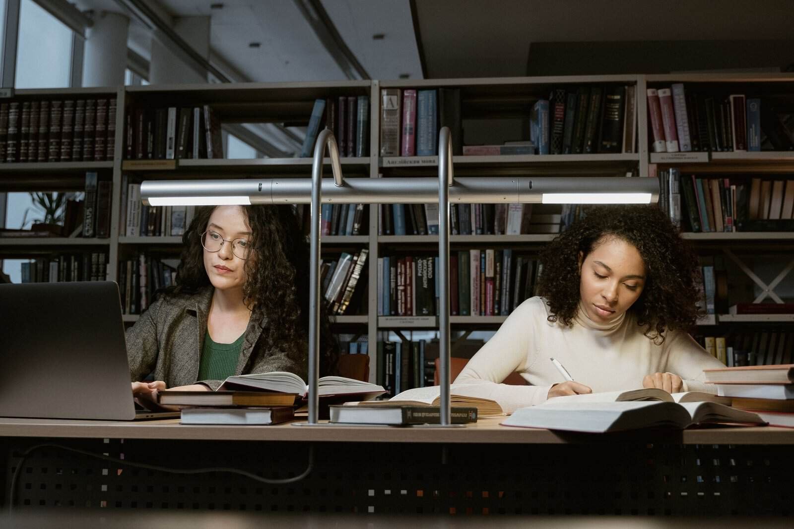 Zwei Studentinnen lesen an einem Bibliothekstisch – APA und Harvard im Vergleich